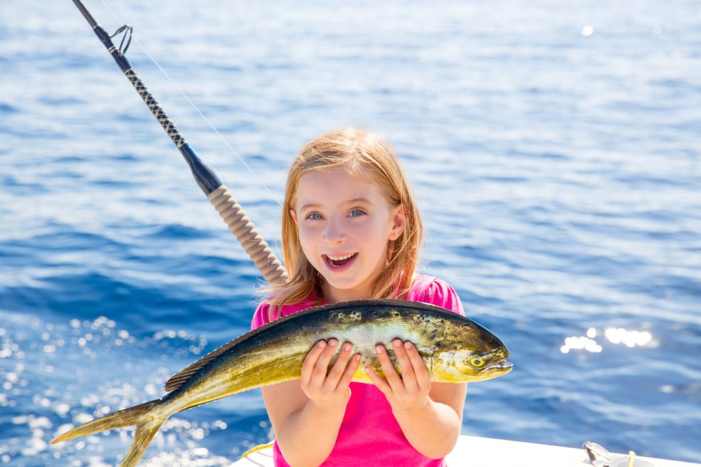 Blond kid girl fishing Dorado Mahi mahi fish happy with trolling catch on boat deck
