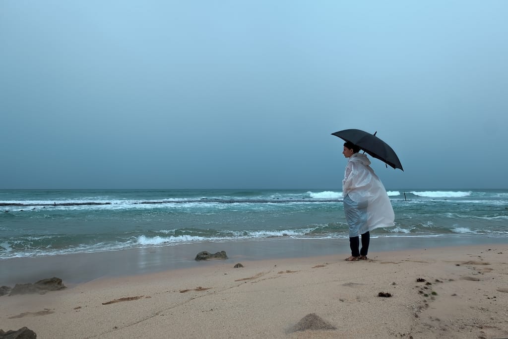 Young woman walking with an umbrella in front of ocean in rainy weather True Southern Accent